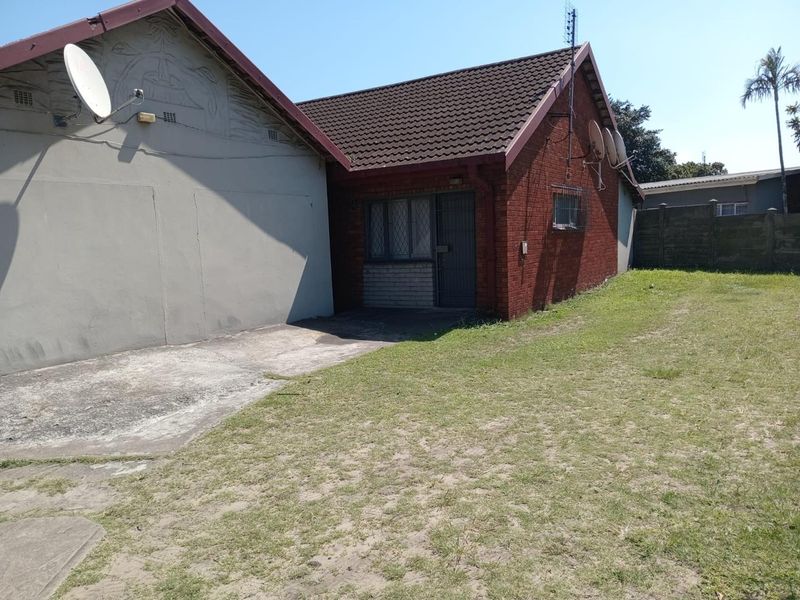 Rear view of the property featuring a brick facade, concrete driveway, and a private lawn area with security features installed.