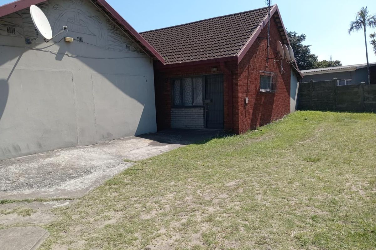 Rear view of the property featuring a brick facade, concrete driveway, and a private lawn area with security features installed.
