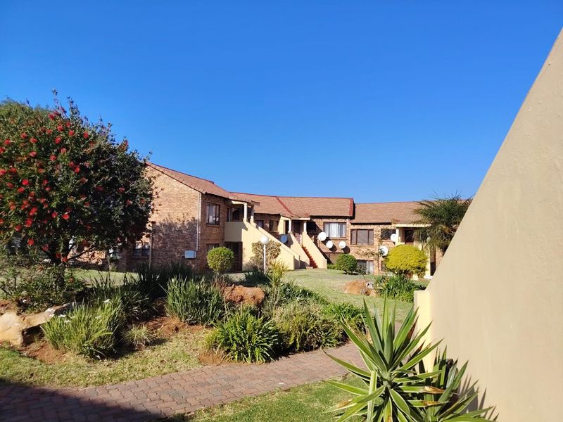 A view of the rear exterior of the townhouse complex, featuring face brick construction, tiled roofing, and well-maintained communal garden areas with paved walkways.