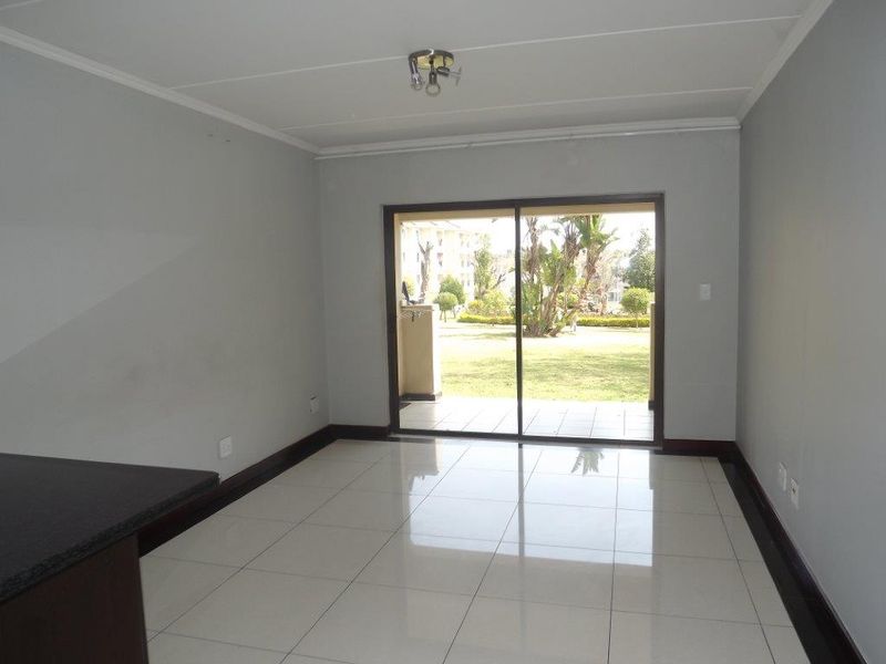 An empty, well-lit living area featuring neutral tiled flooring and a large sliding glass door providing access to the outdoor patio and garden.