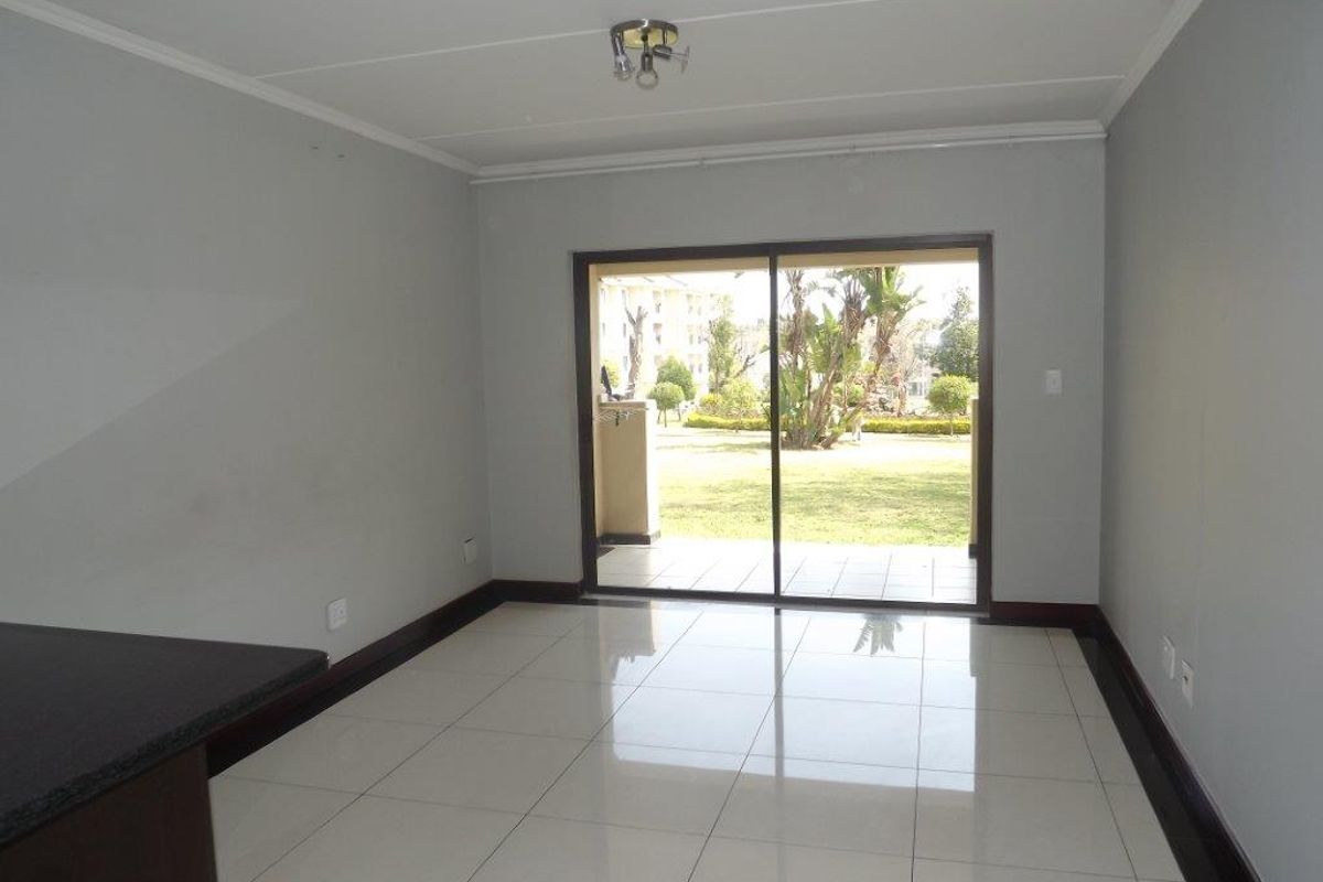 An empty, well-lit living area featuring neutral tiled flooring and a large sliding glass door providing access to the outdoor patio and garden.