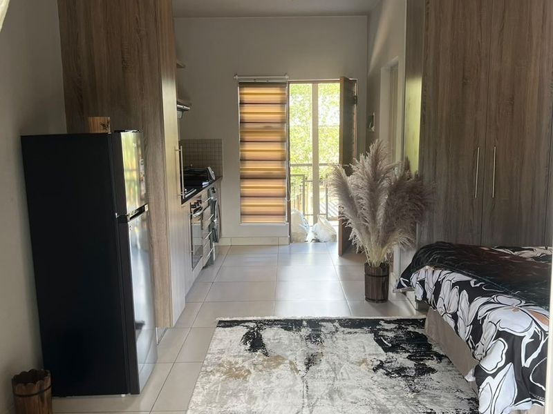 An open-plan studio apartment featuring tiled flooring, built-in cabinetry, and a compact kitchen area with direct access to a balcony.