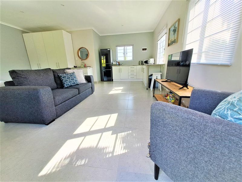 An open-plan living area featuring a compact kitchen with built-in cabinetry, tiled flooring, and ample natural light from multiple windows.