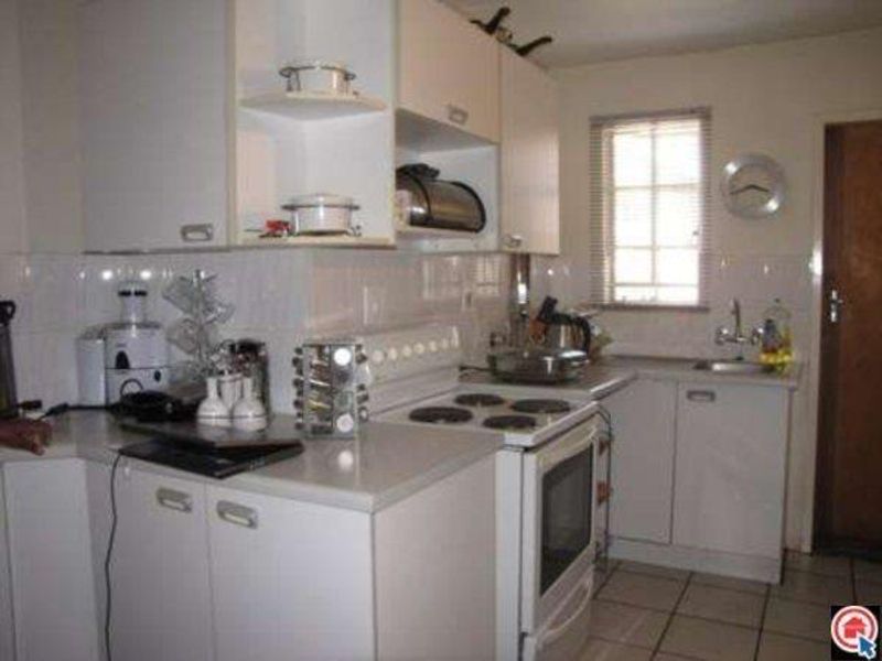A functional kitchen featuring white built-in cabinetry, an electric stove with oven, tiled backsplash, and a stainless steel sink with tiled flooring.