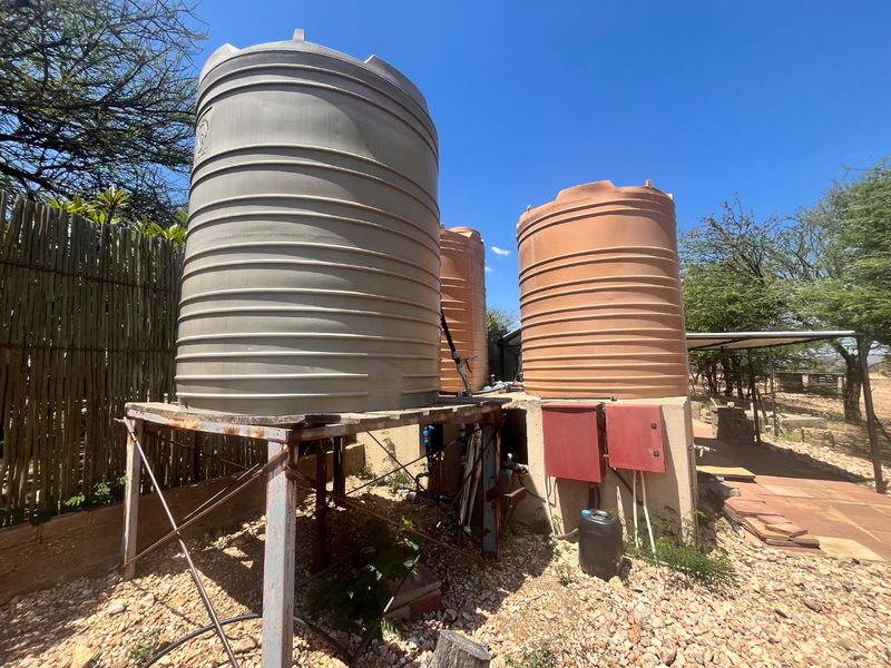Outdoor utility area featuring multiple large water storage tanks mounted on a metal support structure with integrated electrical control boxes.