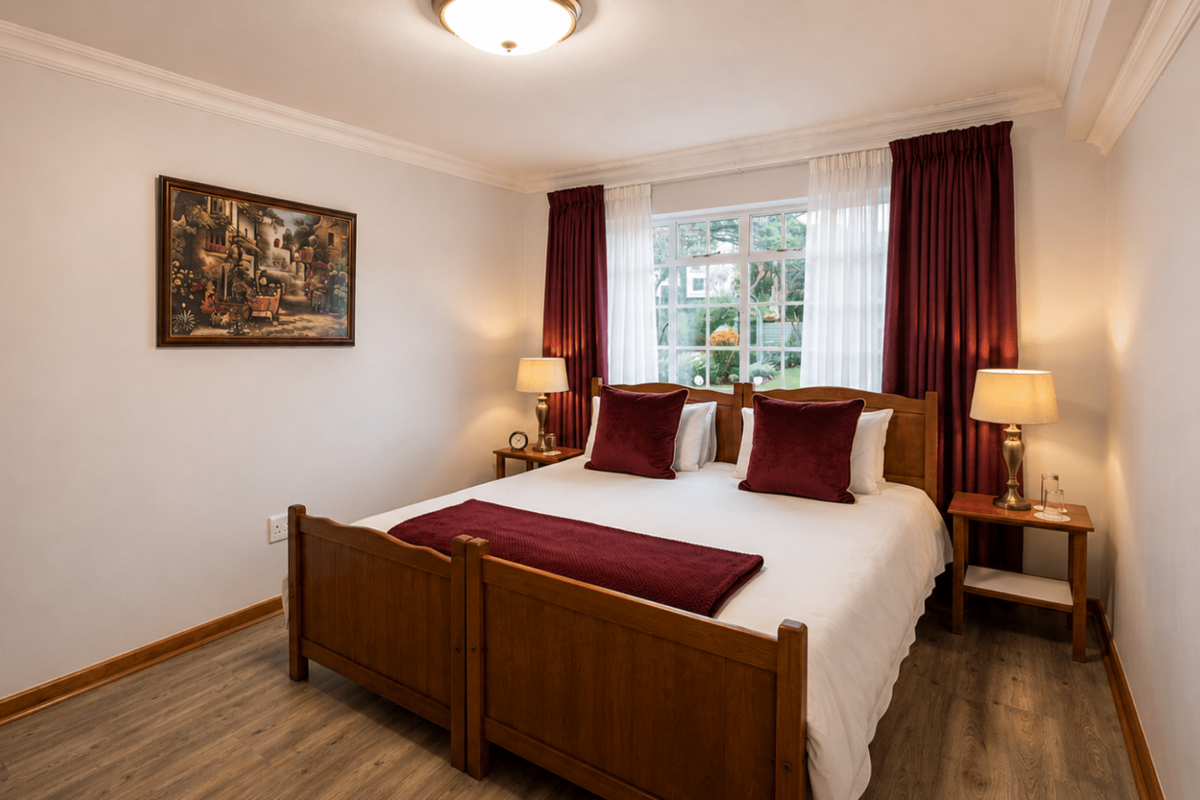 A well-maintained bedroom featuring wood-look laminate flooring, crown molding, and a large window with garden views.