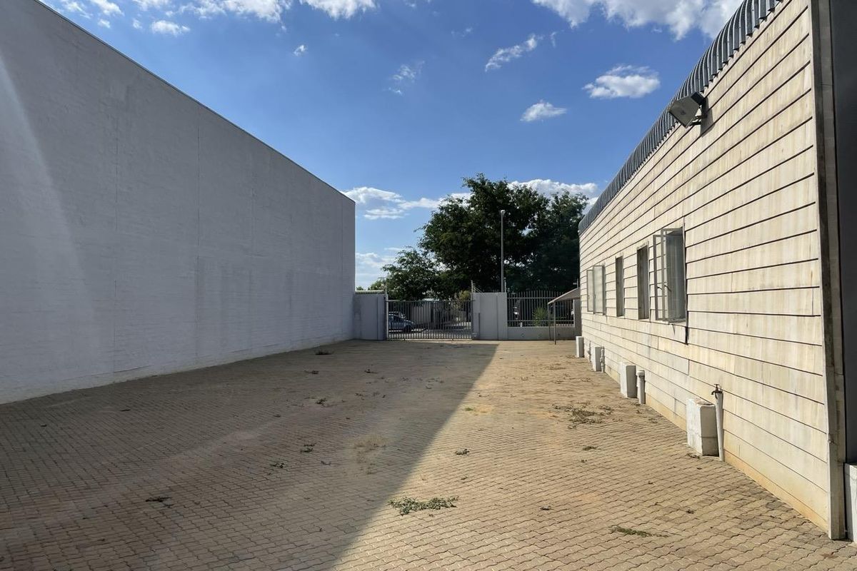 Exterior side yard of an industrial property featuring paved ground, perimeter walling, and security fencing with a gated entrance.
