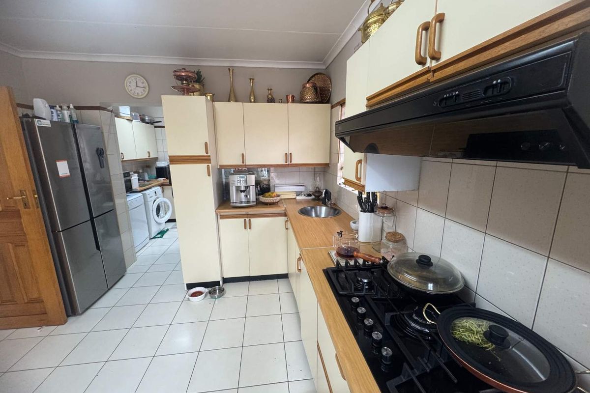 Functional kitchen featuring built-in cabinetry, gas hob with extractor fan, and an adjoining laundry area with tiled flooring throughout.