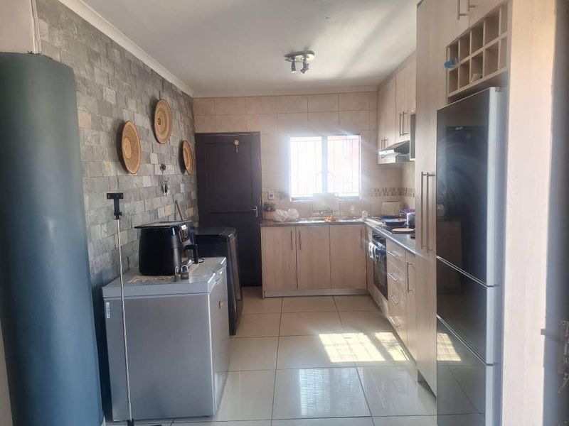A functional kitchen featuring light wood cabinetry, a stone-cladding feature wall, tiled flooring, and integrated storage solutions.
