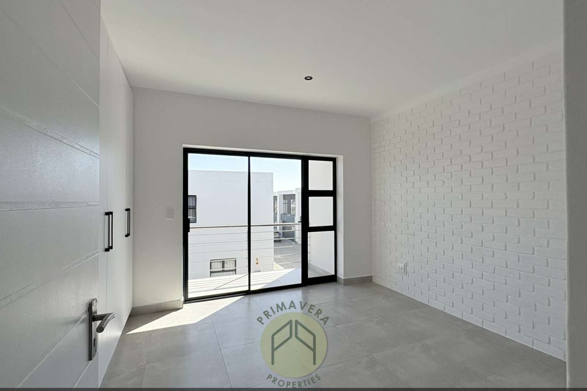A bright, modern bedroom featuring large sliding glass doors leading to a balcony, built-in cupboards, and a decorative white brick feature wall.