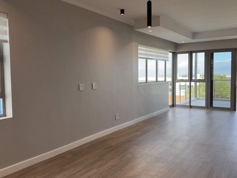 A bright, modern, and empty living room featuring laminate flooring, recessed lighting, and large sliding doors leading to a private balcony.