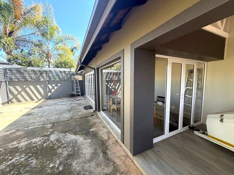 Rear exterior view featuring a covered patio with tiled flooring, aluminium sliding doors, and a paved courtyard area.