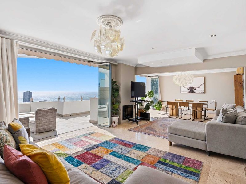 Spacious open-plan living and dining area featuring stone flooring, a built-in fireplace, and seamless flow to a balcony with expansive ocean views.