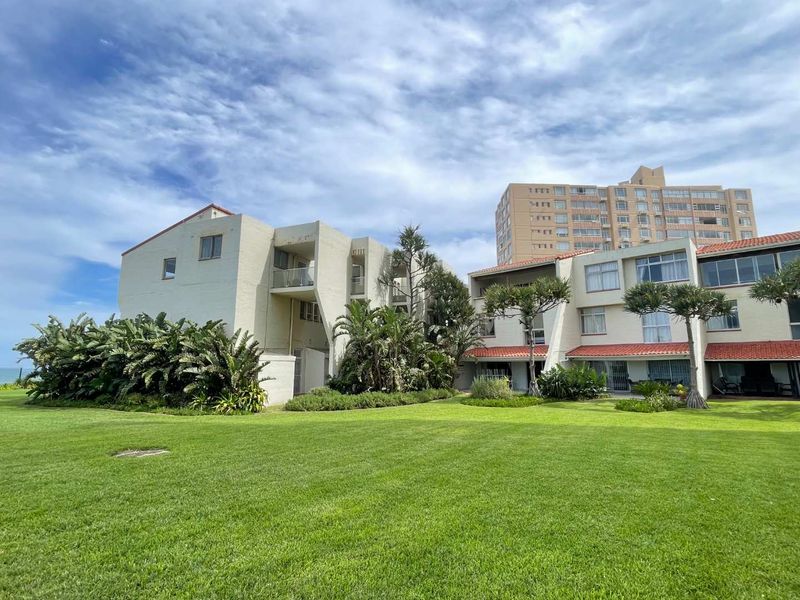 A view of the apartment complex rear facade featuring landscaped lawns, terracotta roof tiles, and private balconies.