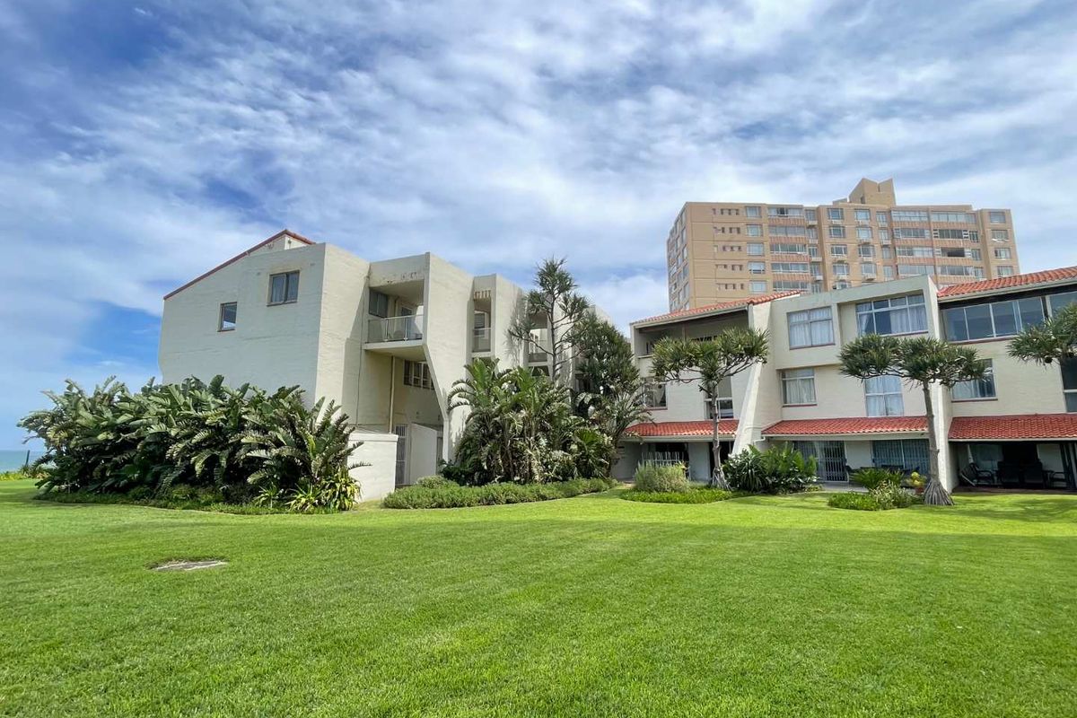 A view of the apartment complex rear facade featuring landscaped lawns, terracotta roof tiles, and private balconies.