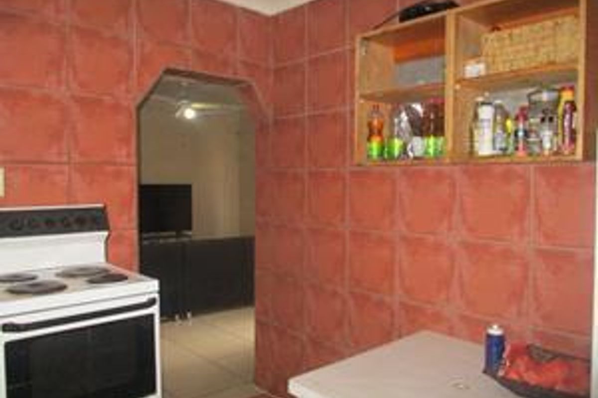 A functional kitchen area featuring terracotta-style wall tiles, built-in wall cabinetry, and a freestanding electric stove.