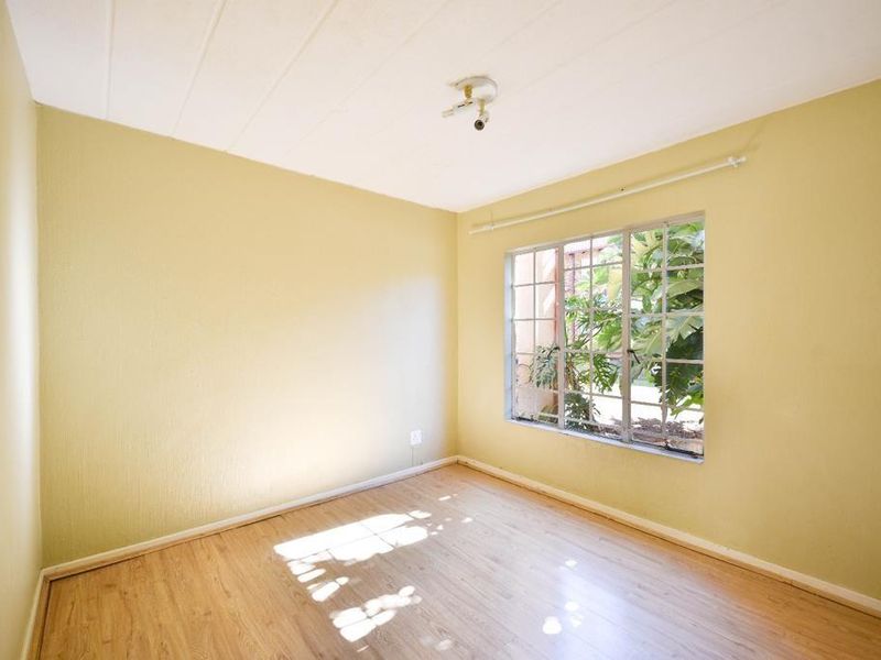 An empty bedroom featuring laminate flooring, yellow-toned walls, and a steel-framed window with security bars, offering a blank canvas for renovation.