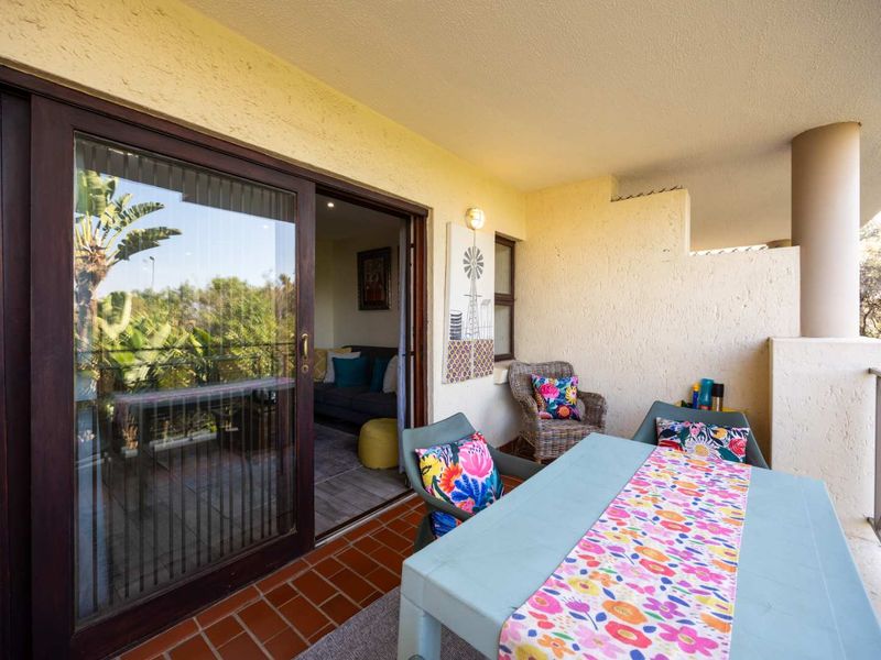 A covered balcony featuring terracotta floor tiles, textured walls, and a sliding glass door providing access to the interior living space.