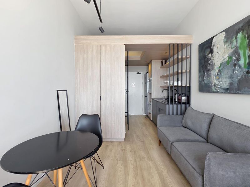 Modern open-plan living area featuring light wood-tone cabinetry, integrated kitchenette with open shelving, and durable laminate flooring in a compact, well-designed layout.