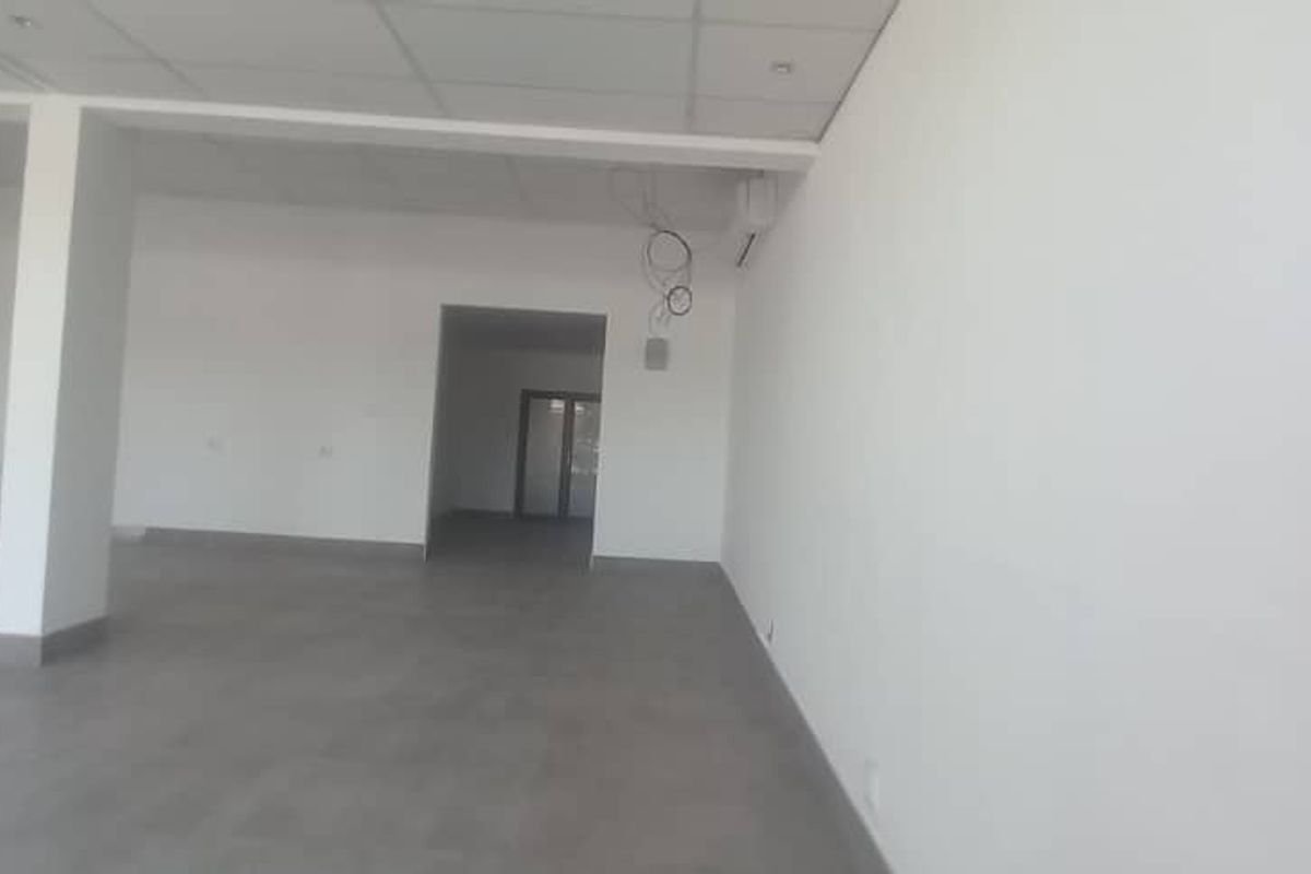 An empty, open-plan retail space featuring tiled flooring, a suspended ceiling with recessed lighting, and a structural column.