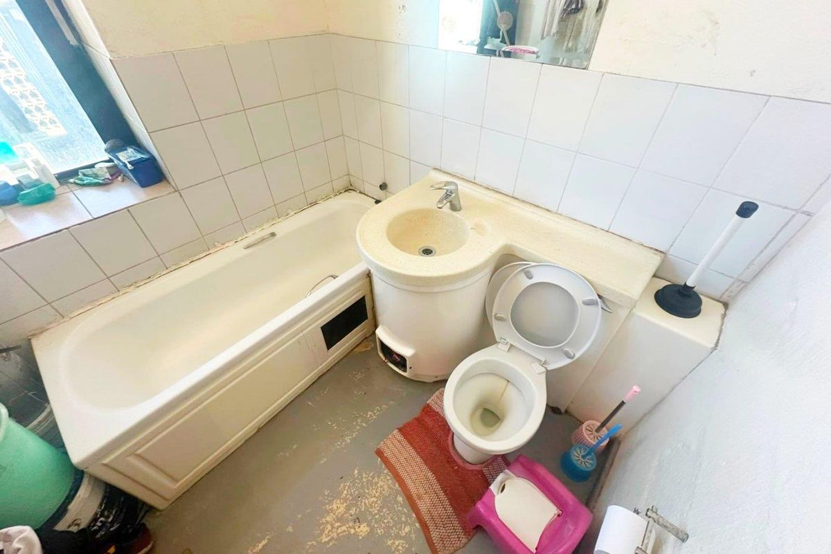 A compact bathroom featuring an integrated vanity basin, bathtub, and toilet, requiring cosmetic updates and refurbishment of finishes.