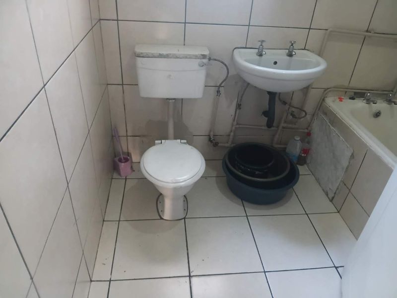 A dated bathroom featuring a standard toilet, pedestal basin, and bathtub with full-height ceramic wall tiling and floor tiles.