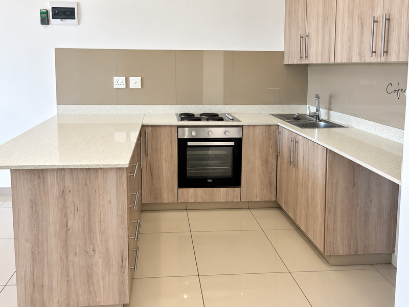 Modern kitchen featuring light wood-grain cabinetry, stone countertops, integrated electric oven and hob, and sleek glass splashbacks in a clean, open-plan layout.