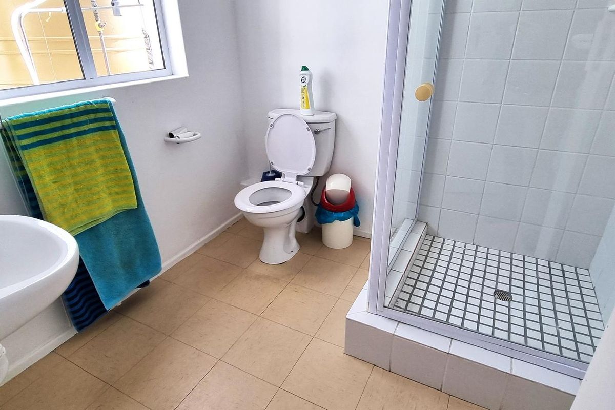 A functional office bathroom featuring a shower cubicle, pedestal basin, and toilet with tiled flooring and white wall finishes.