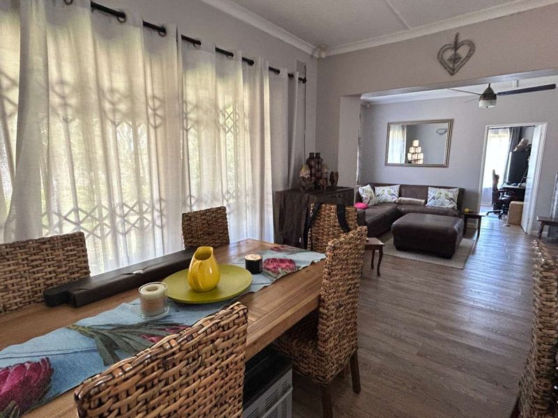 Open-plan living and dining area featuring laminate flooring, ceiling fan, and large windows with security gates, creating a connected and functional living space.