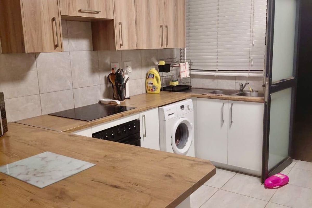 A functional kitchen featuring wood-look cabinetry, laminate countertops, a built-in oven and hob, and tiled flooring with integrated laundry appliance space.