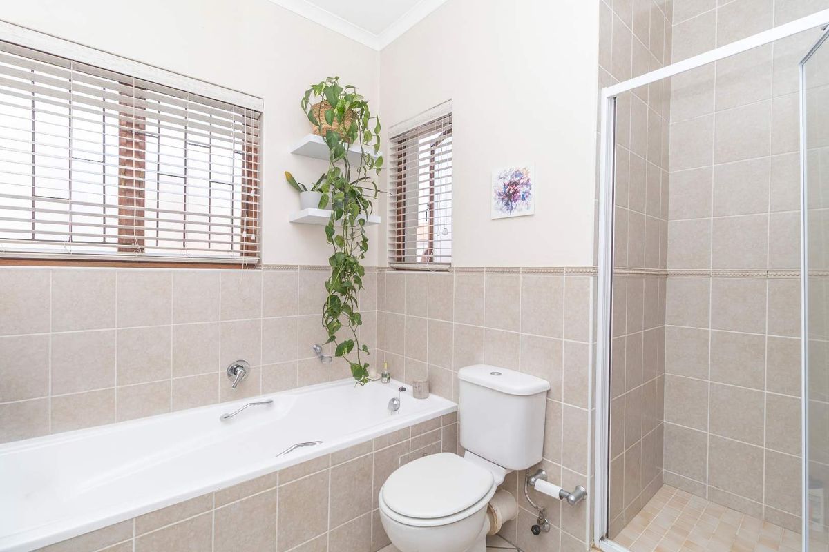 A well-maintained bathroom featuring a built-in bathtub, separate shower enclosure, and neutral wall tiling with functional window blinds.