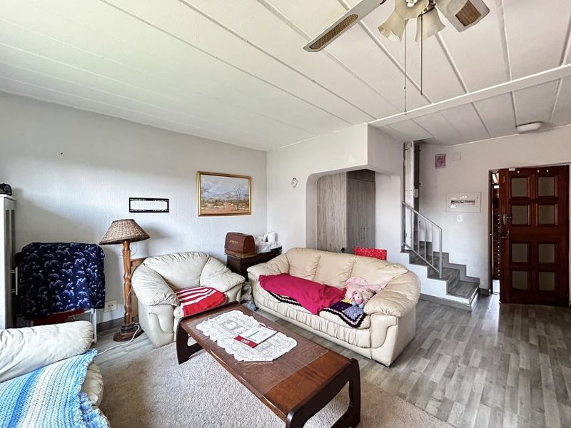A living room featuring laminate flooring, a ceiling fan, and an integrated staircase leading to the upper level.