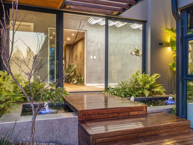 A modern outdoor patio area featuring timber decking, integrated water features, and large sliding glass doors leading into the home.
