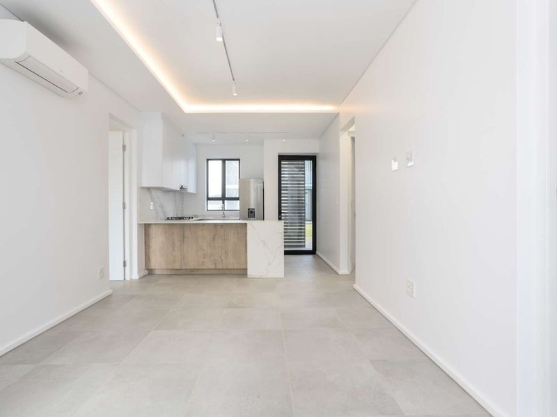 A bright and modern open-plan living and kitchen area featuring neutral tiled flooring, recessed lighting, and high-quality built-in cabinetry with stone countertops.