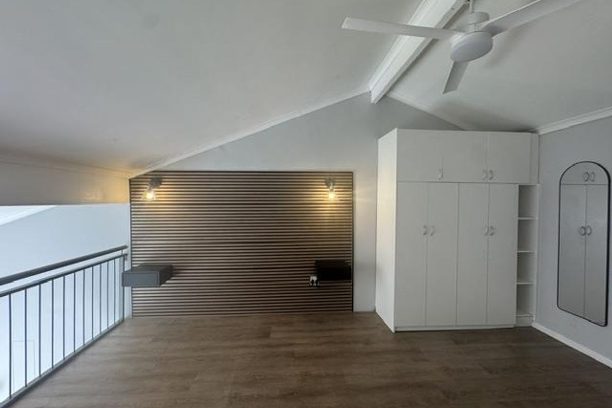Spacious loft-style bedroom featuring a slatted timber feature wall, built-in wardrobes, ceiling fan, and modern laminate flooring with a metal balustrade overlooking the lower level.