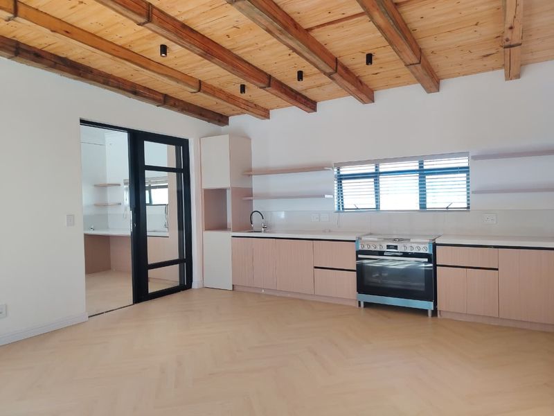 Modern kitchen featuring herringbone timber flooring, exposed wooden ceiling beams, sleek cabinetry, and a freestanding oven, with an adjacent scullery area.