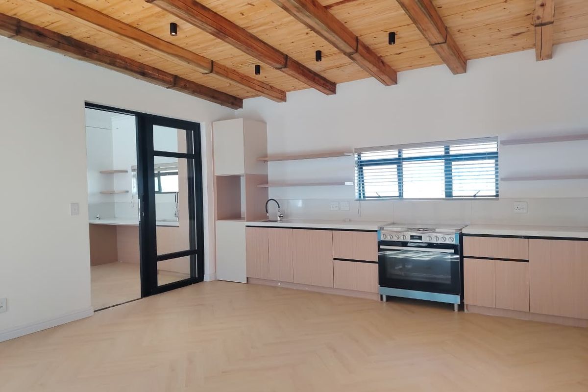 Modern kitchen featuring herringbone timber flooring, exposed wooden ceiling beams, sleek cabinetry, and a freestanding oven, with an adjacent scullery area.