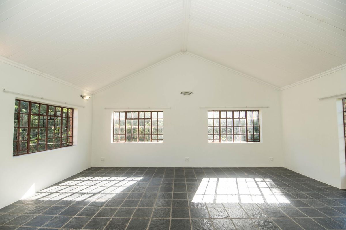 A spacious, empty living area featuring a high vaulted ceiling, slate tile flooring, and multiple timber-framed windows providing ample natural light.