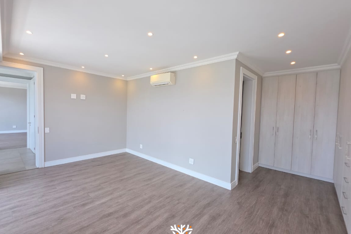 Spacious bedroom featuring light wood-look laminate flooring, built-in cupboards, recessed ceiling lighting, and a wall-mounted air conditioning unit.