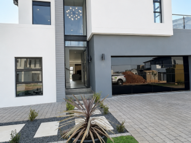 A modern double-story home featuring a sleek facade, paved driveway, double garage, and a well-maintained front garden.