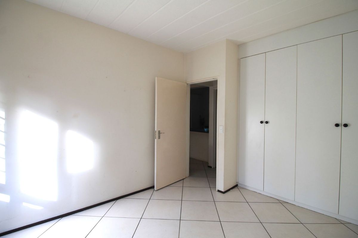 An empty bedroom featuring white built-in cupboards, tiled flooring, and a panelled ceiling, offering a clean and neutral space ready for personalization.