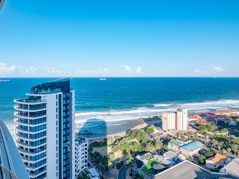 Elevated coastal view overlooking the ocean, beach, and surrounding urban landscape from a high-rise apartment balcony.