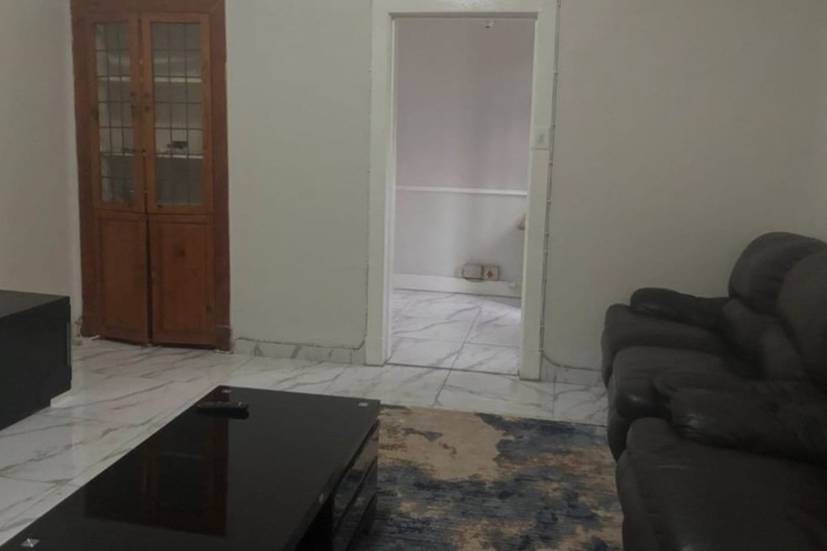 A living room featuring marble-look floor tiles and a built-in wooden display cabinet, with a doorway leading to an adjacent room.