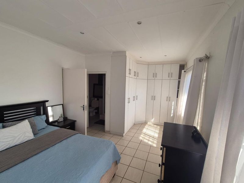 A bedroom featuring built-in cupboards, tiled flooring, recessed lighting, and direct access to an en-suite bathroom.