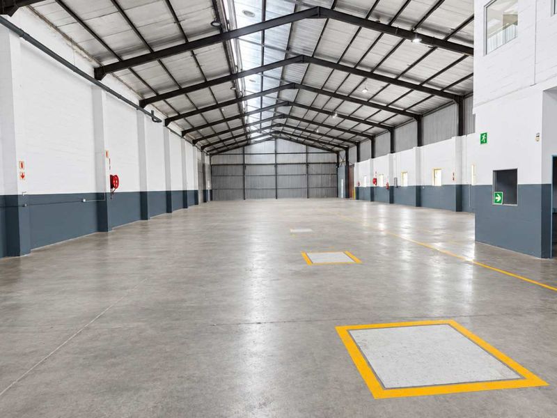 Spacious industrial warehouse unit featuring high ceilings with exposed steel trusses, durable concrete flooring, and clean painted masonry walls.