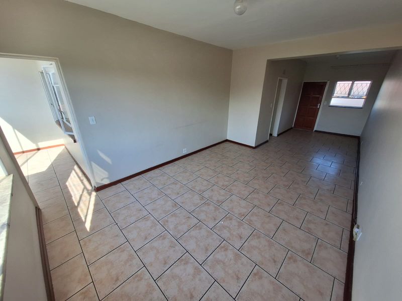 An empty open-plan living area featuring neutral wall tones and tiled flooring, providing a versatile space with direct access to the entrance.