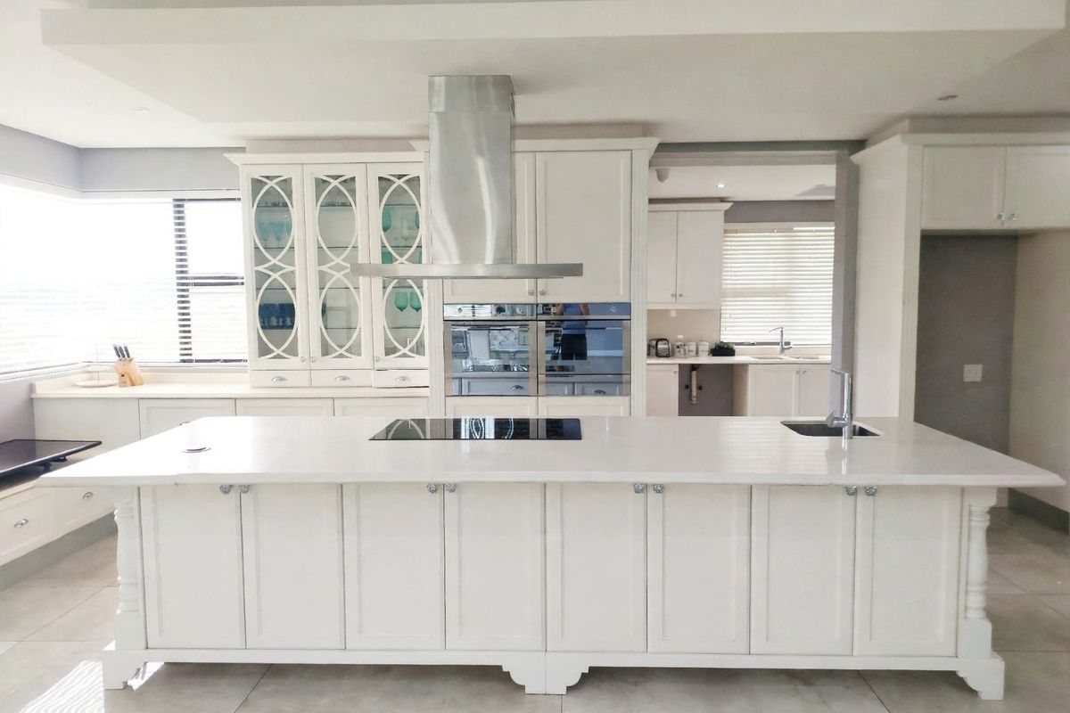 Spacious modern kitchen featuring a large central island with integrated cooktop and sink, high-end built-in appliances, and elegant white cabinetry.