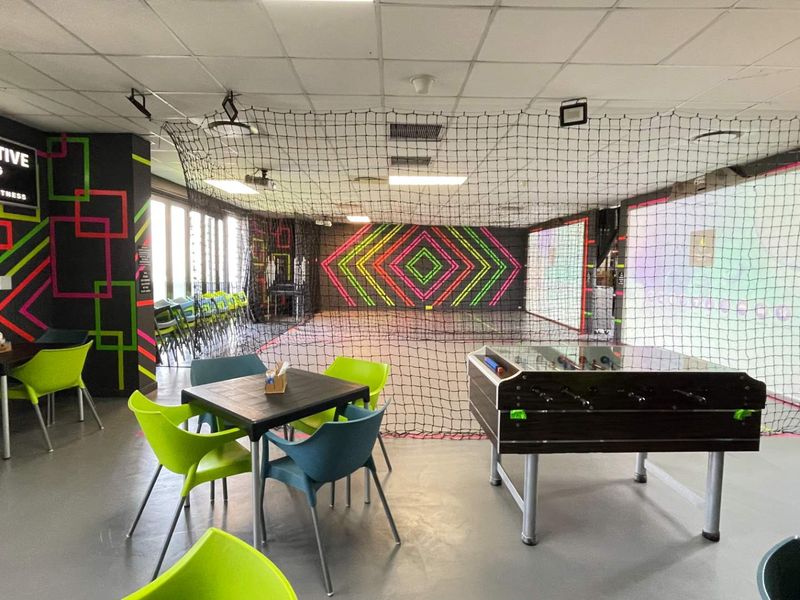 An indoor sports and gaming facility featuring safety netting, projector screens, and a suspended ceiling, designed for interactive entertainment.