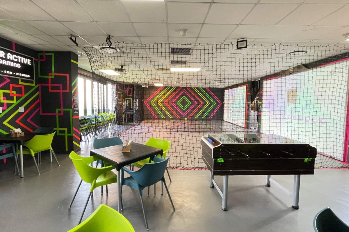 An indoor sports and gaming facility featuring safety netting, projector screens, and a suspended ceiling, designed for interactive entertainment.