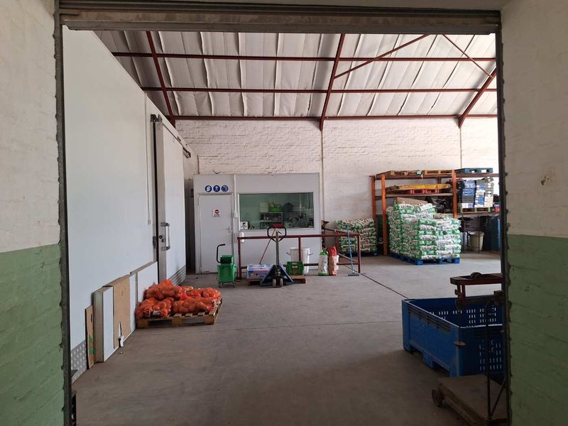 Industrial warehouse space featuring exposed steel roof trusses, concrete flooring, and a built-in office partition, suitable for storage or light manufacturing operations.